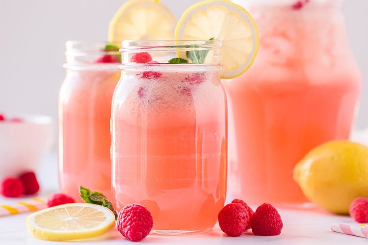 Two mason jar glasses of homemade raspberry lemonade with lemon wheels and fresh raspberries