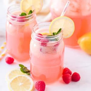 Pink raspberry flavored lemonade in mason jar glasses with striped straws, lemon slices, and fresh raspberries