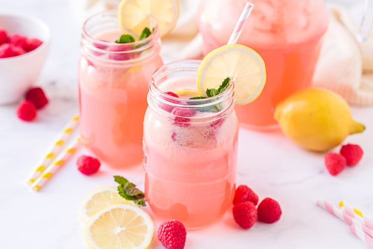 Pink raspberry flavored lemonade in mason jar glasses with striped straws, lemon slices, and fresh raspberries