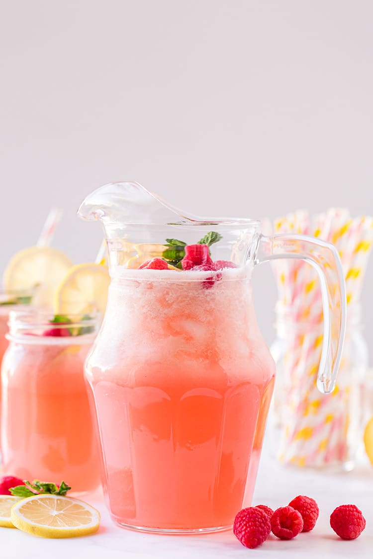 Large pitcher of fresh raspberry lemonade with lemons and raspberries