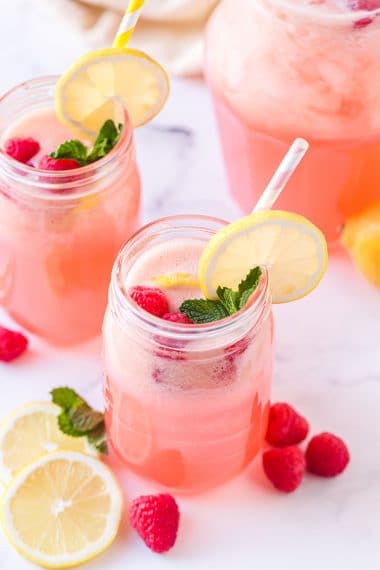 Homemade raspberry lemonade in mason jar glasses with striped straws, lemon slices, raspberries, and mint garnish