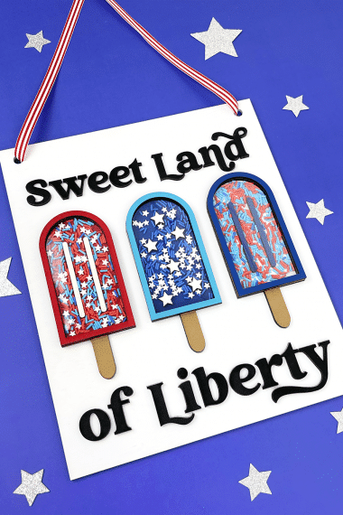 "Sweet Land of Liberty" sign with popsicles on a blue background with silver stars