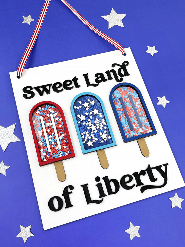 "Sweet Land of Liberty" sign with popsicles on a blue background with silver stars