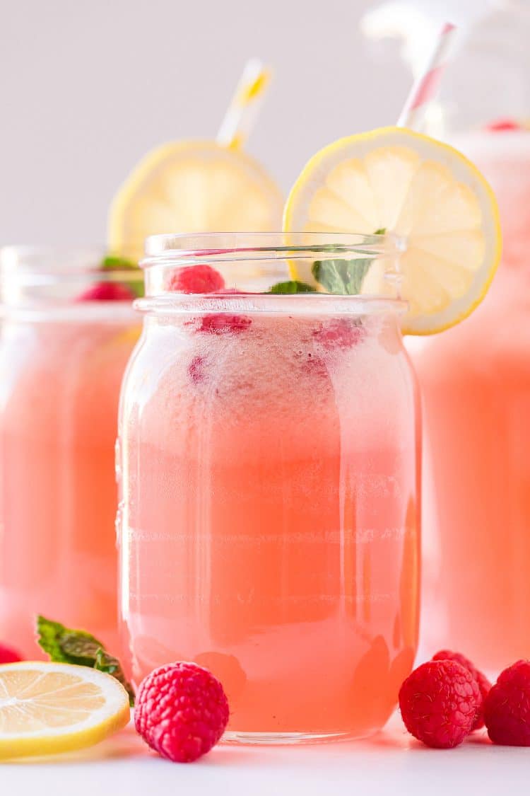 Mason jar glass filled with pink raspberry lemonade and garnished with a lemon slilce
