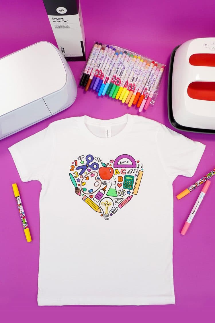 Back to school coloring shirt on a purple background surrounded by fabric markers and Cricut supplies