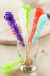 Five colorful homemade rock candy sticks in a display glass