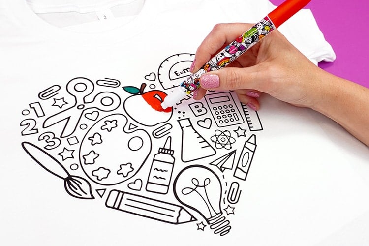 Close up of hand with red fabric marker coloring a back to school shirt