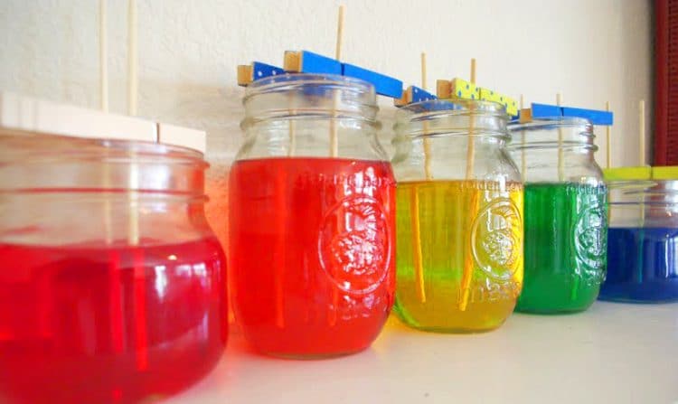 rainbow mason jars filled with sugar solution and sticks for homemade rock candy