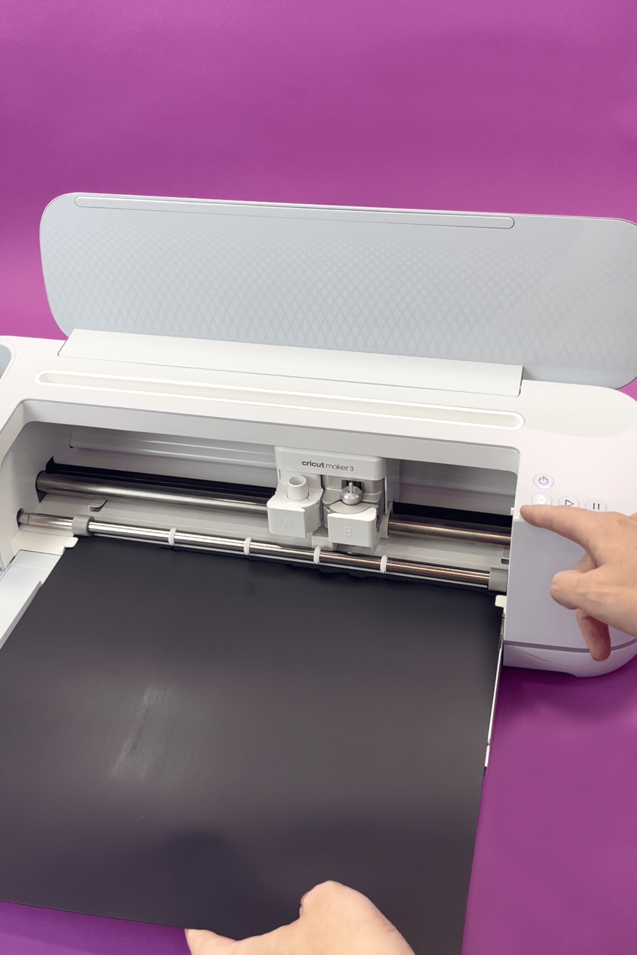 Hands loading black Smart Iron-On into a Cricut Maker 3 on purple background