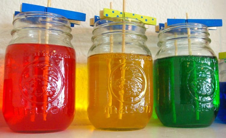 three mason jars full of colorful sugar solution and wooden skewers