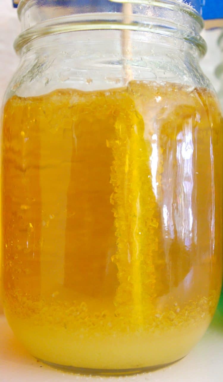 rock candy crystals developing on a stick in a mason jar of yellow sugar solution