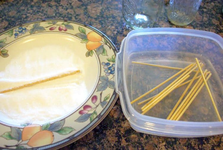 wooden skewers soaking in a bowl of water next to a plate of sugar