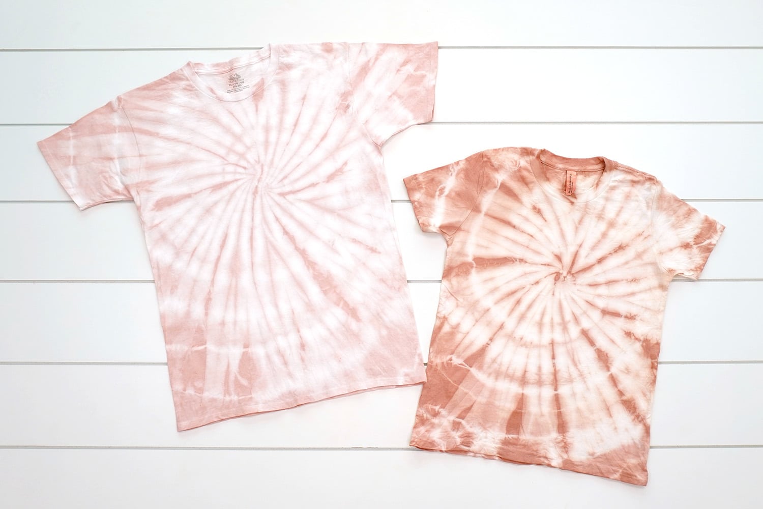 two spiral tie-dye shirts on a white background, one blush pink color and one a peachy pink
