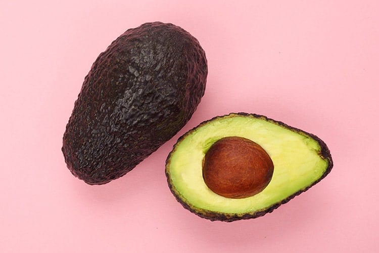 Whole and halved avocados on pink background