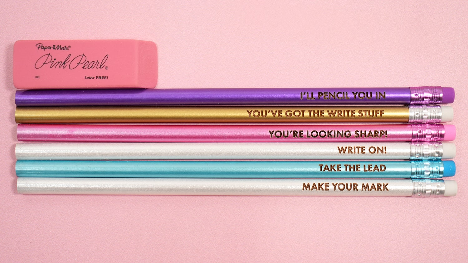 Six engraved pencils with pencil pun phrases on a pink background