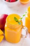 Close up overhead shot of mango smoothie with mint leaf garnish and striped straw