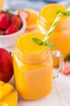 Mango smoothie in mason jar glass garnished with mint leaves and a green and white striped straw