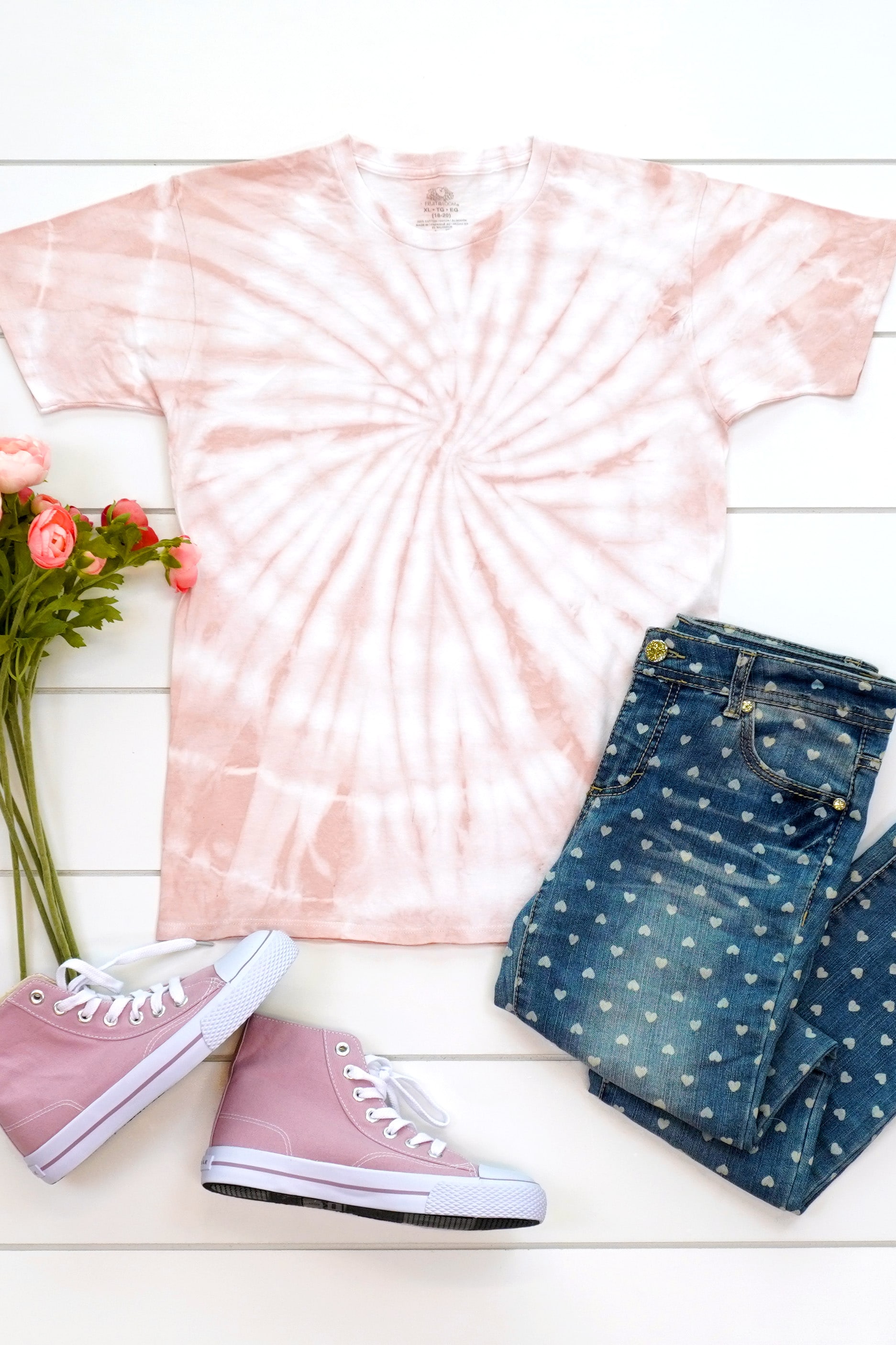 Blush pink spiral tie-dyed shirt made with avocado dye staged with an outfit and flowers on a white background