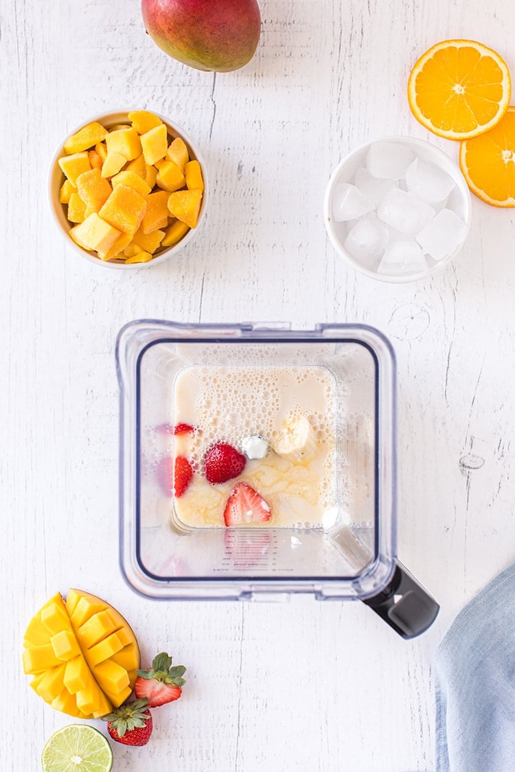 Strawberries, banana, almond milk, and yogurt mango smoothie ingredients in blender