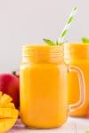 Mango smoothie in glass with mint sprig and green striped straw