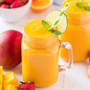 Mango smoothie in a mason jar glass with a lime wheel and a green and white striped straw