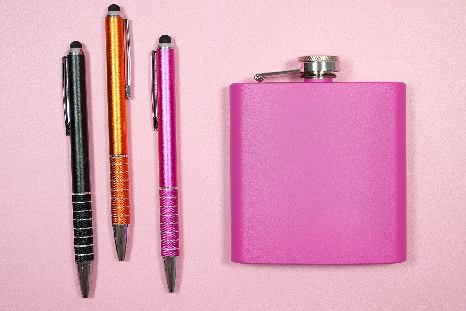 Aluminum barrel pink, black, and orange pens and a pink flask on a light pink background