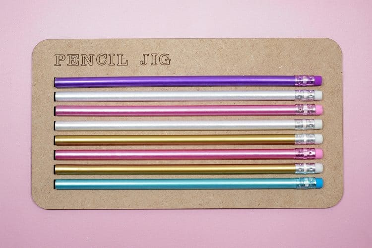 Colorful pencils in a pencil jig on a pink background