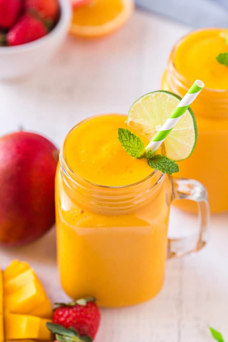 Mango smoothie in a mason jar glass with a lime wheel and a green striped straw