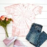 Blush pink spiral tie-dyed shirt made with avocado dye staged with an outfit and flowers on a white background