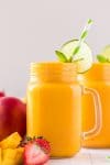 Mango smoothie in a mason jar glass garnished with lime, mint, and a green striped straw