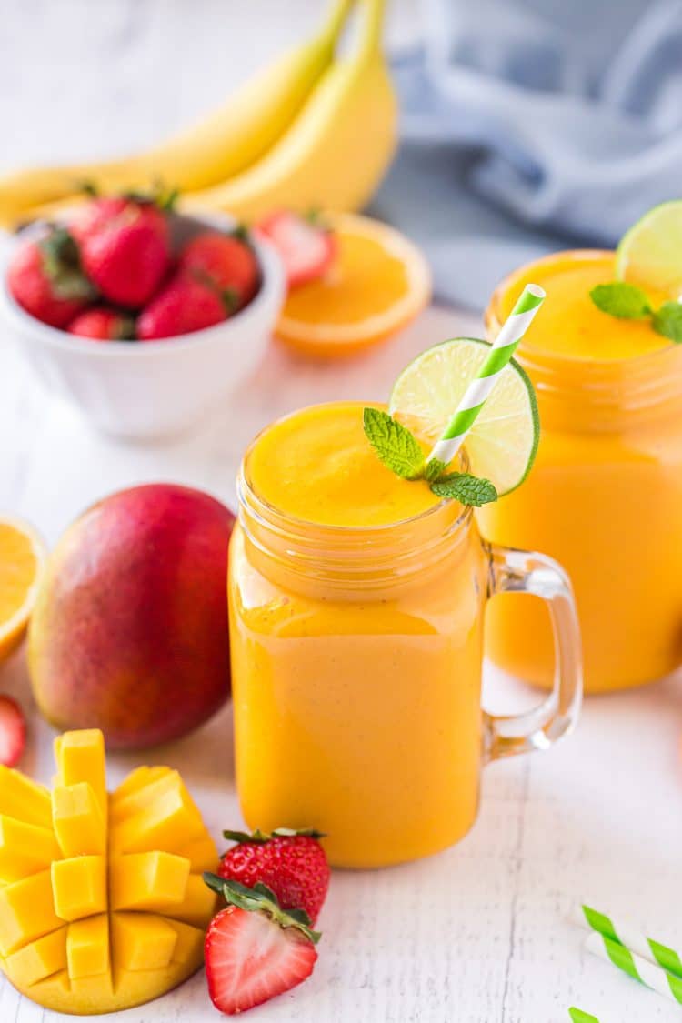 Mango smoothie in a mason jar glass garnished with strawberries, lime, and a green striped straw