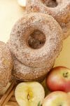 Apple cider donuts with cinnamon sugar topping on yellow background with apples