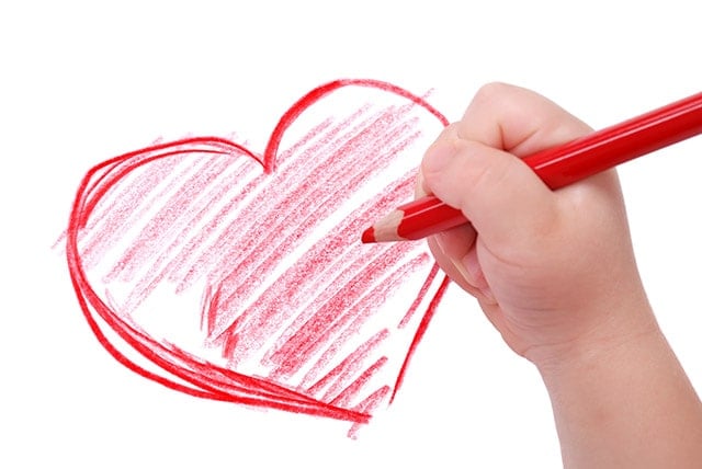 Child's hand with red pencil drawing a heart