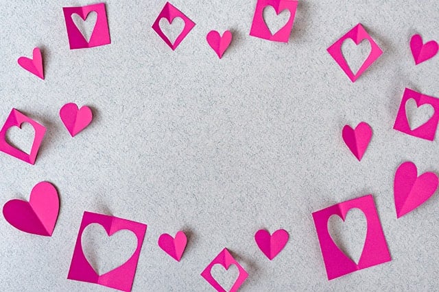 Pink paper hearts and negative-space papers on grey textured background 