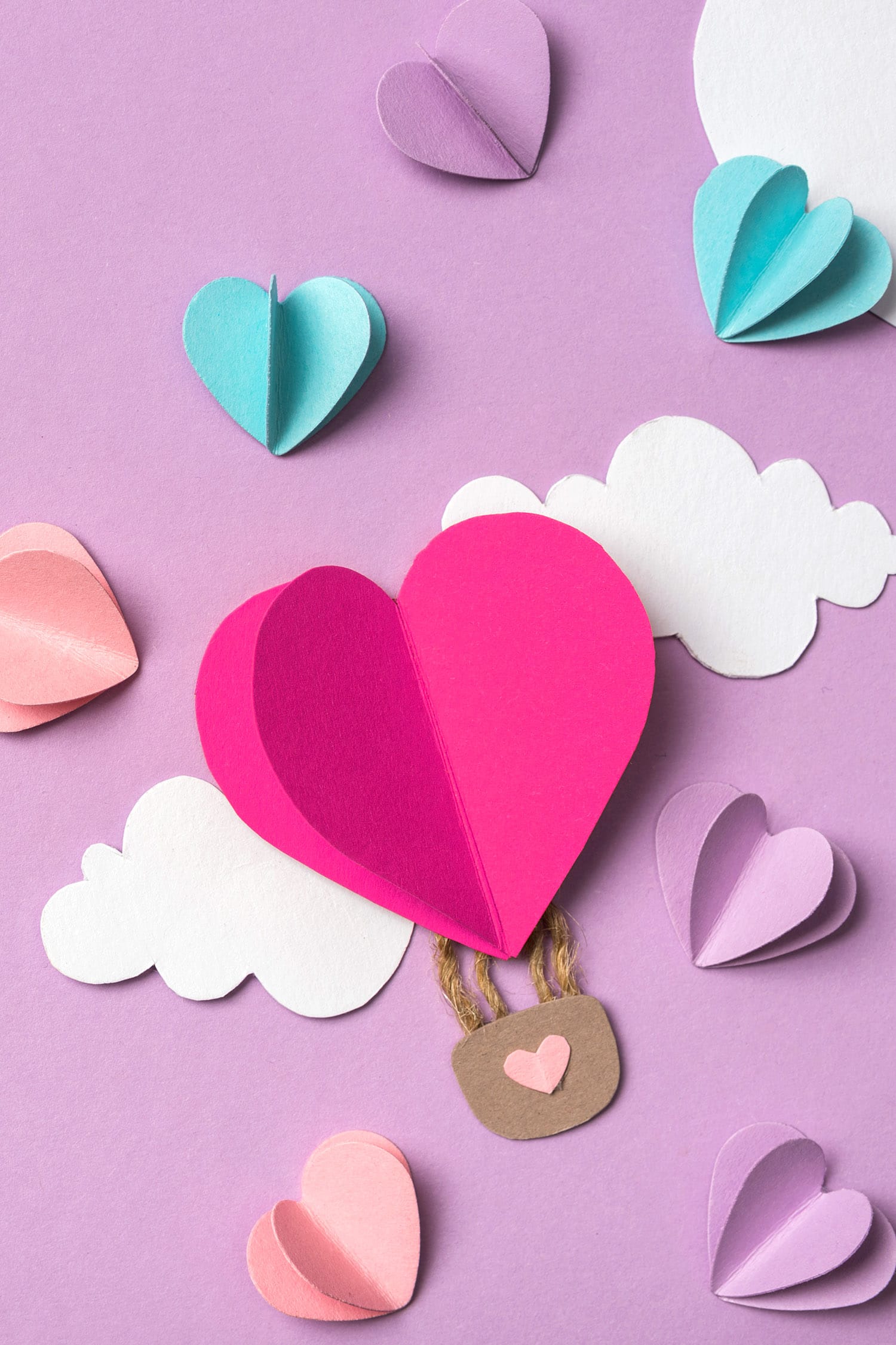 colorful paper hearts and clouds around heart shaped paper hot air balloon on purple background