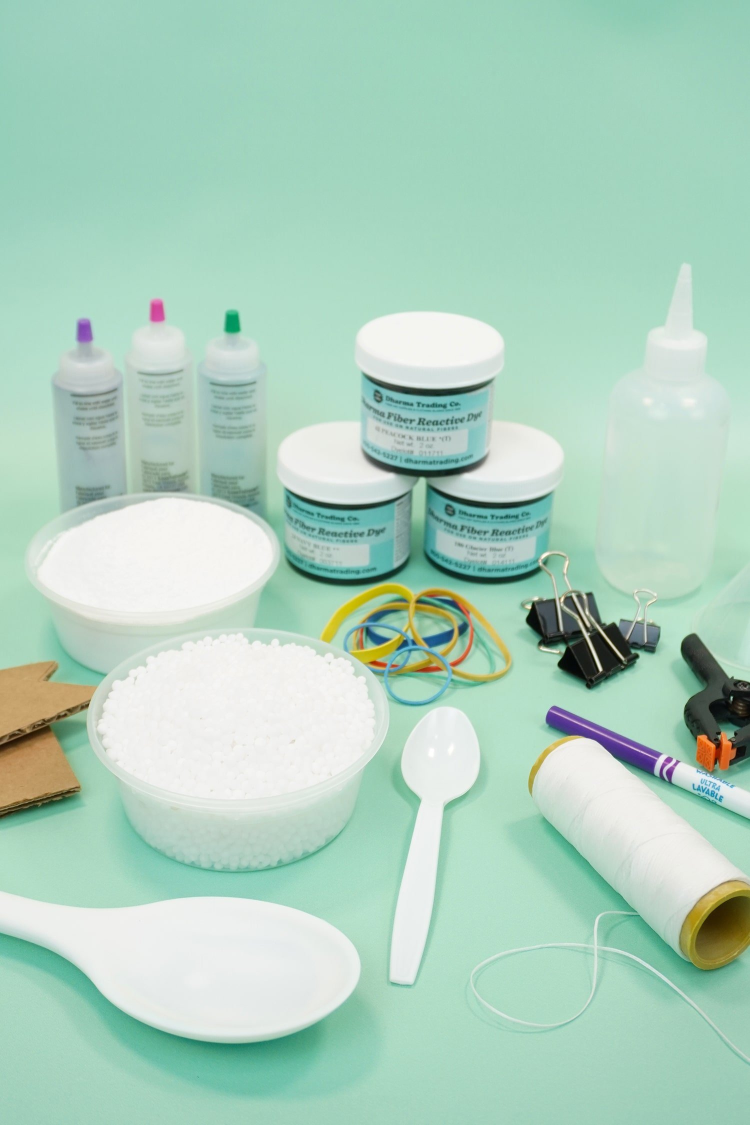 Assorted tie-dye supplies and dye bottles on mint green background