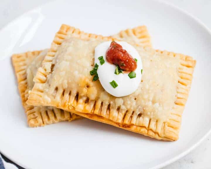 Two taco Pop Tart style pockets on a white plate topped with sour cream and salsa
