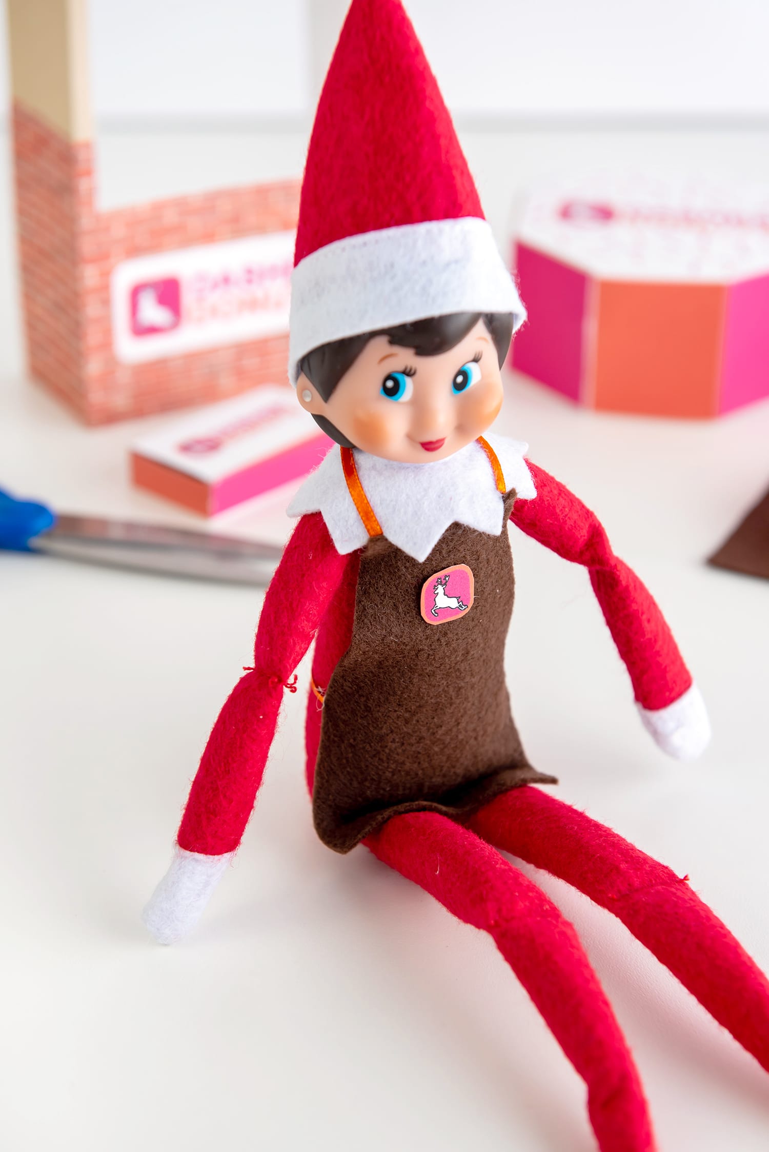 Detail of Elf on the Shelf wearing a felt apron with a Dasher Donuts logo