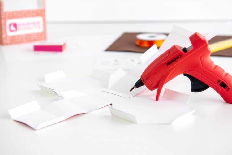 Hot glue gun and folded donut box template on a white background