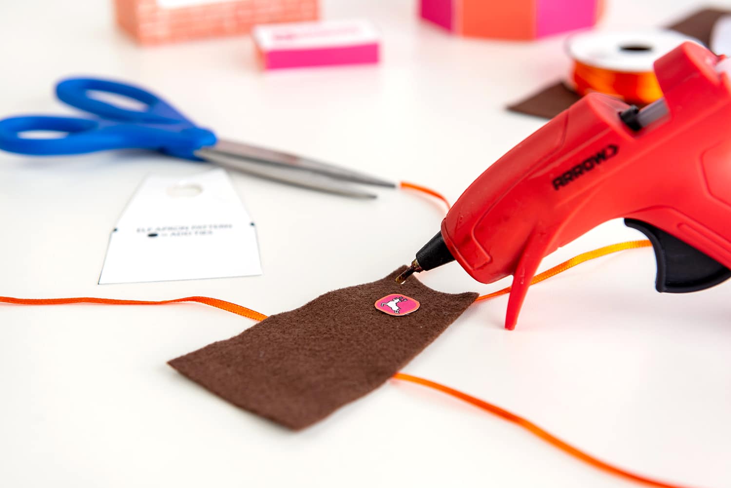 Hot glue gun attaching a Dasher Donuts logo to a felt apron for Elf on the Shelf