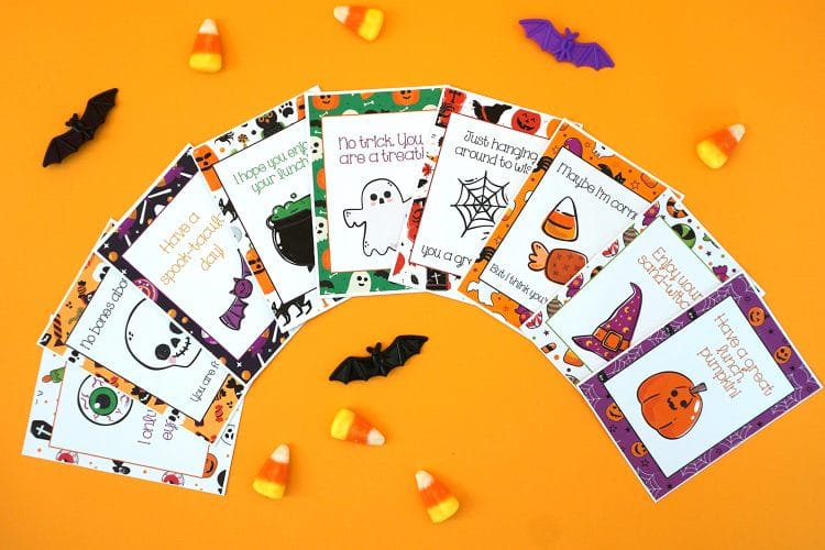 Halloween lunch note cards fanned out on an orange background with candy corn and bats