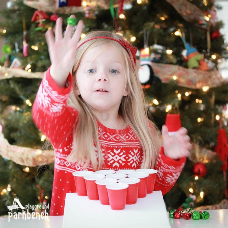 little girl playing jingle bell toss game in front of the Christmas tree 