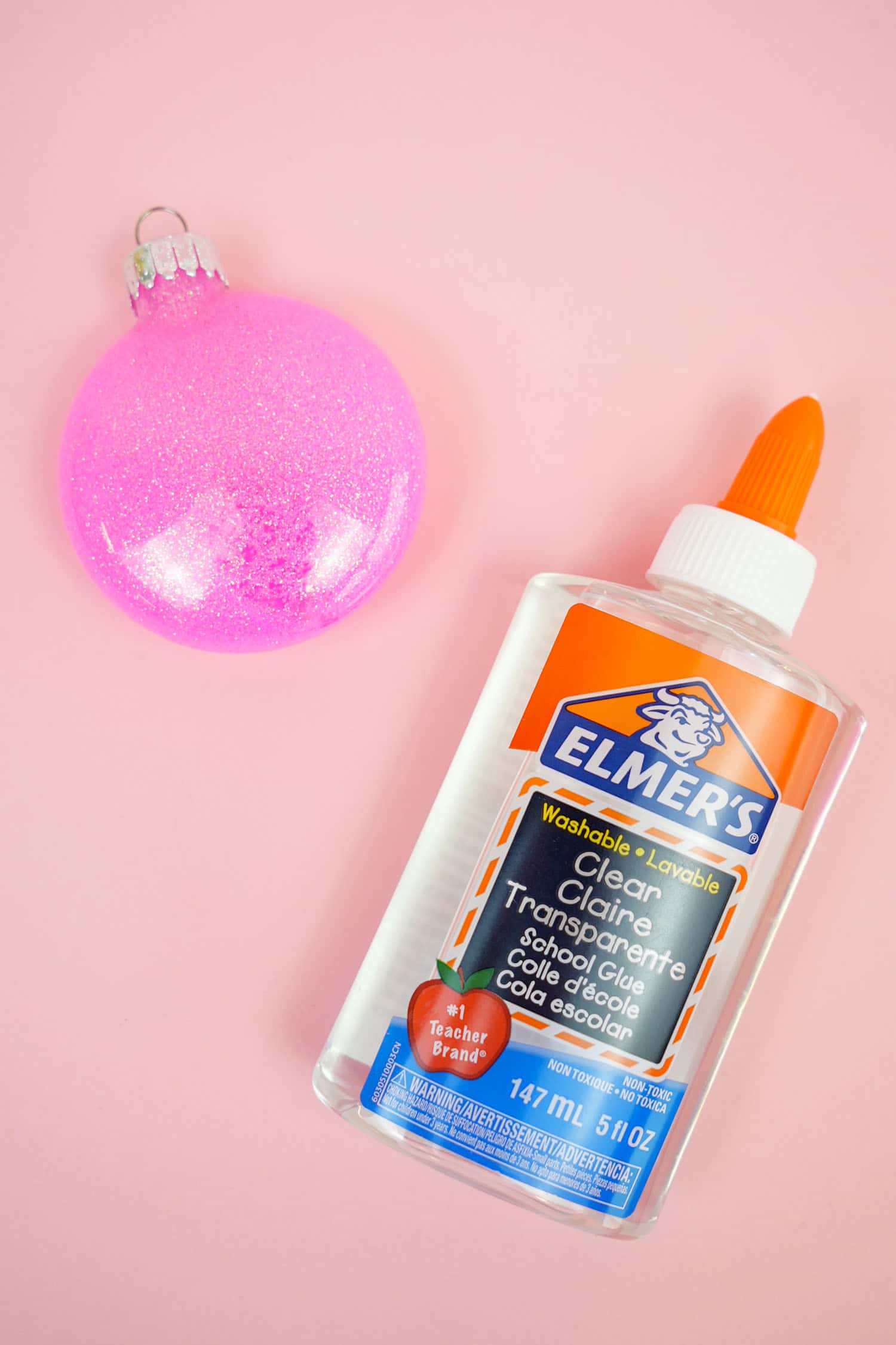 glitter ornaments are sitting on a pink surface with glue