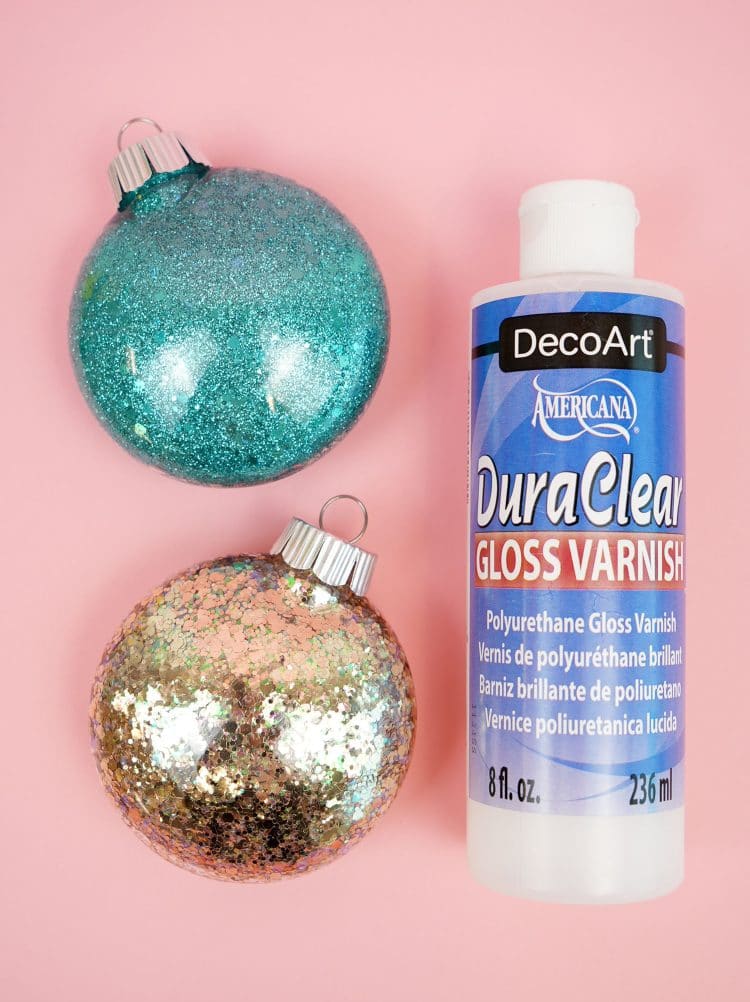 glitter ornaments are sitting on a pink surface with gloss varnish