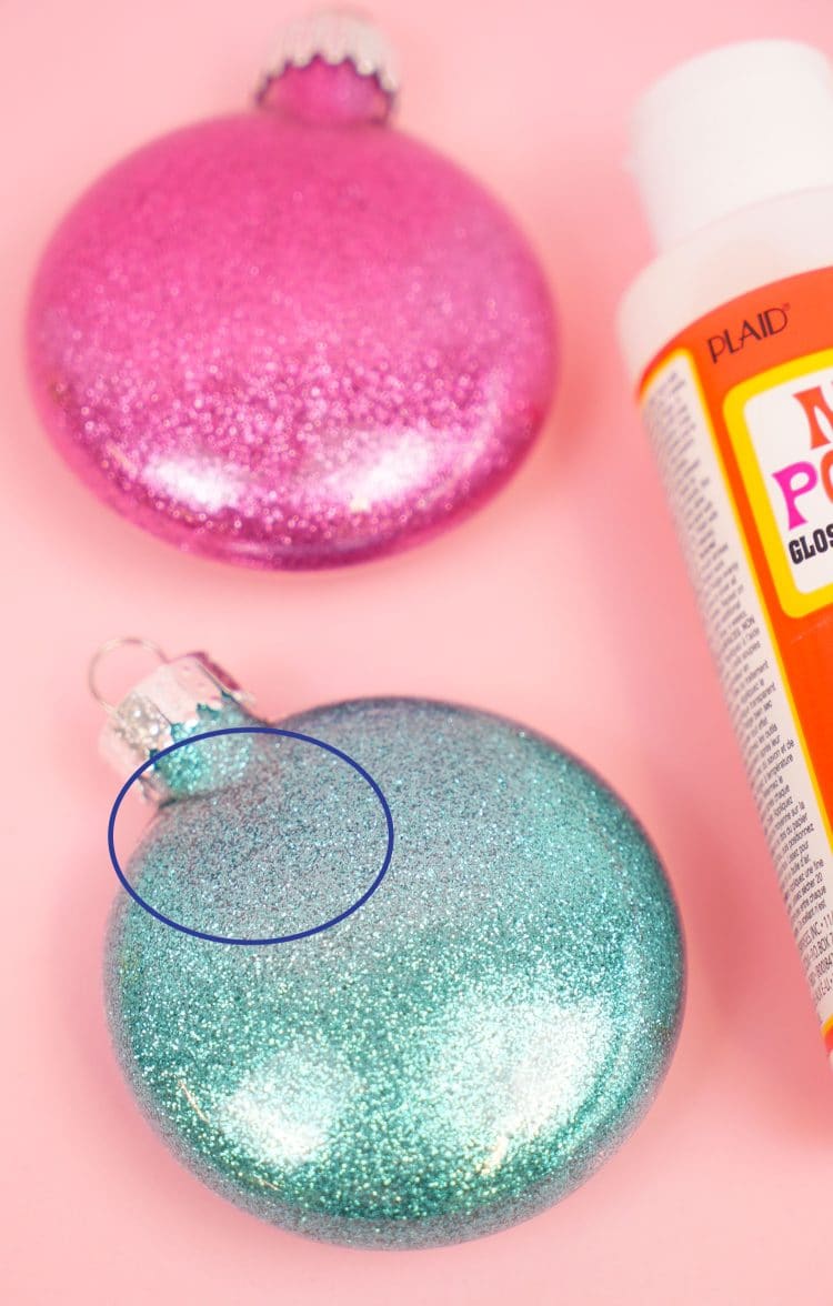 glitter ornaments are sitting on a pink surface with mod podge