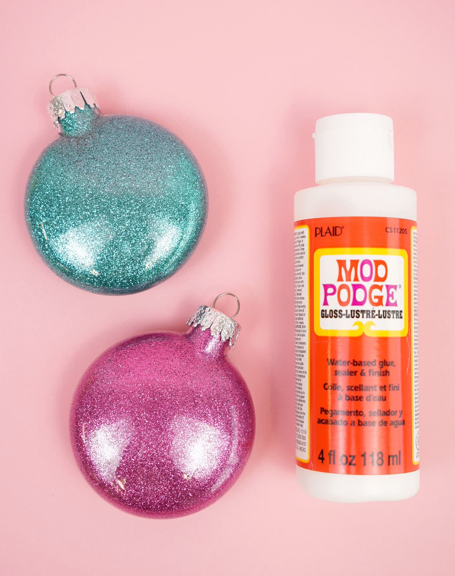 glitter ornaments are sitting on a pink surface with mod podge