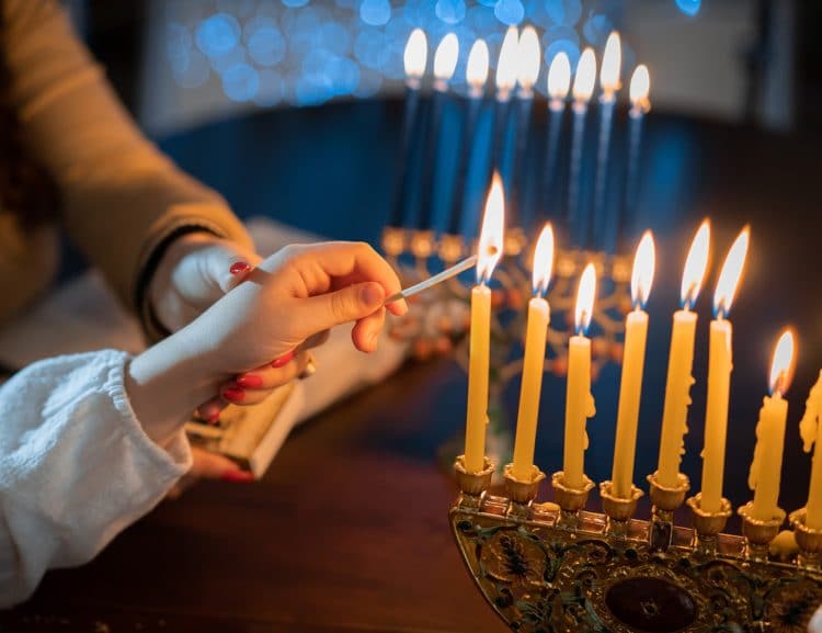 Close up of adult and child's hand lighting a Hanukkah menorah
