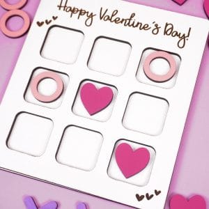 Valentine Tic Tac Toe game made with Glowforge laser SVG file on a lavender background with X's, O's, and pink heart game pieces