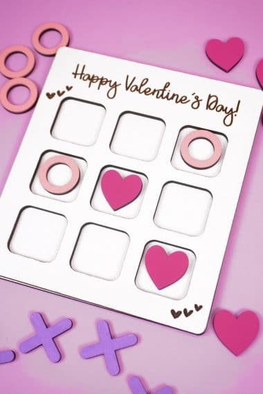 Valentine Tic Tac Toe game made with Glowforge laser SVG file on a lavender background with X's, O's, and pink heart game pieces