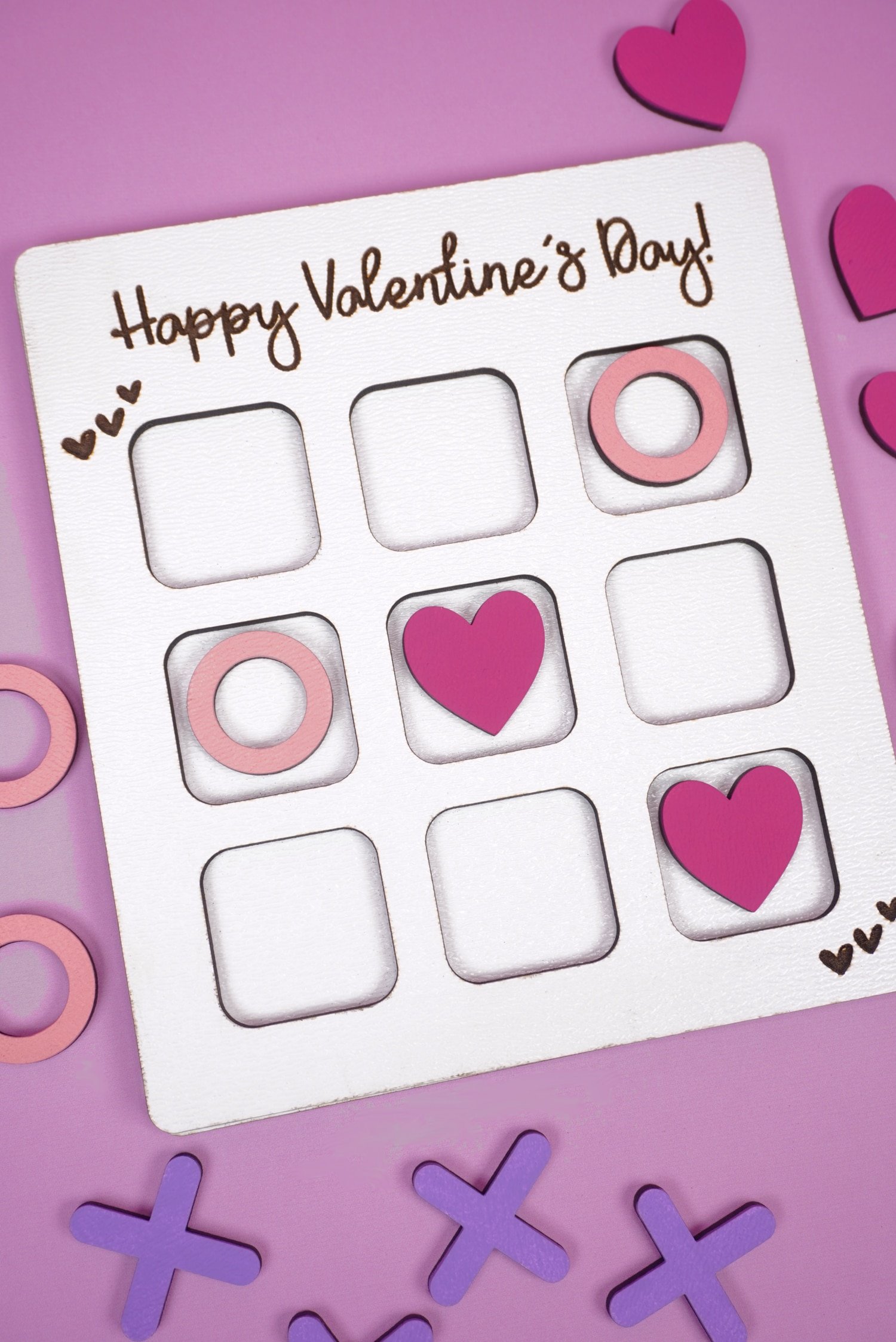 Valentine Tic Tac Toe game made with Glowforge laser SVG file on a light purple background with X's, O's, and pink hearts